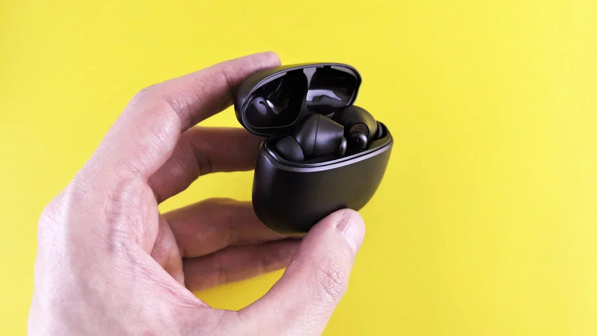 Hand holding black wireless earbuds in open case.