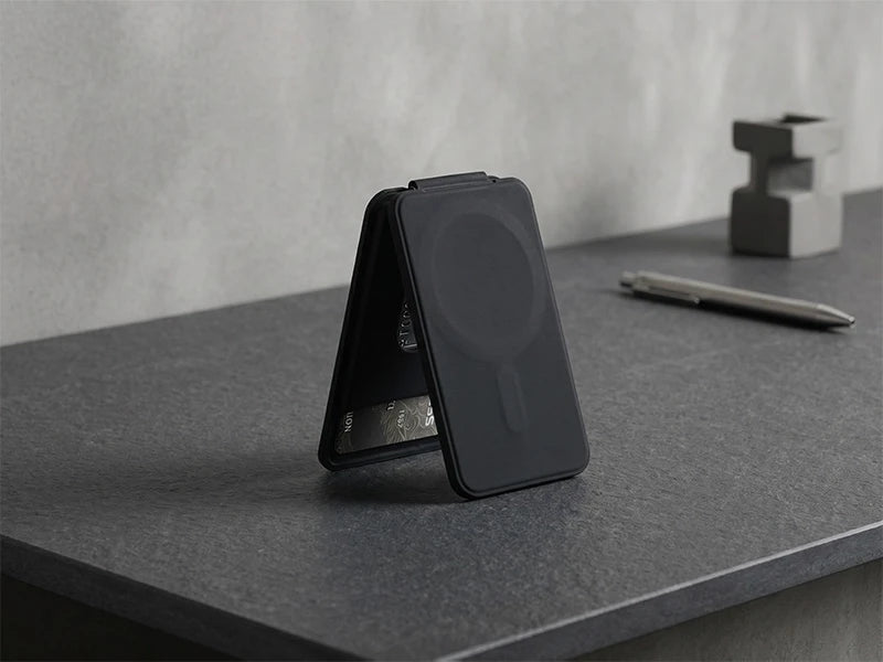 Black card wallet on a gray surface with a pen and a small object in the background.