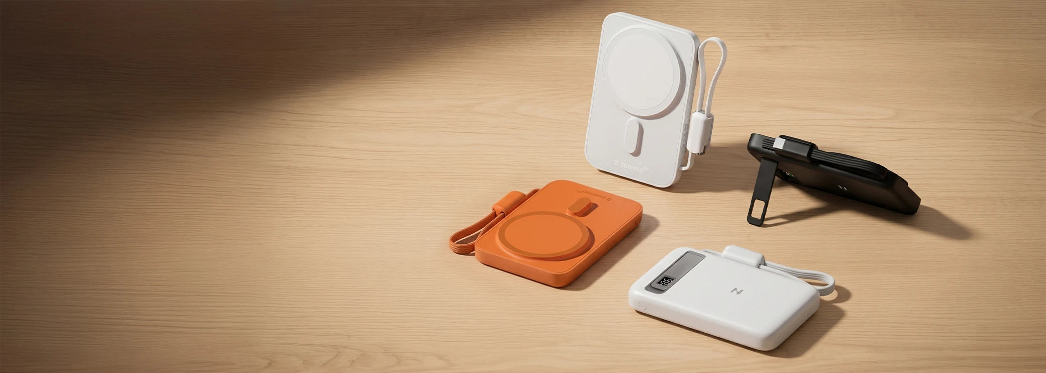Four MagAir power banks in white, black, and orange colorways displayed on a wooden surface.