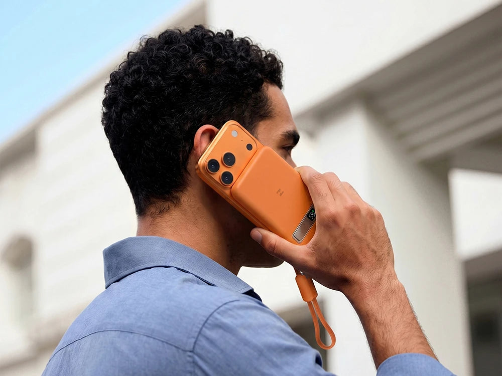 Person holding a smartphone with MagAir magnetic wireless power bank attached to the back, outdoors.