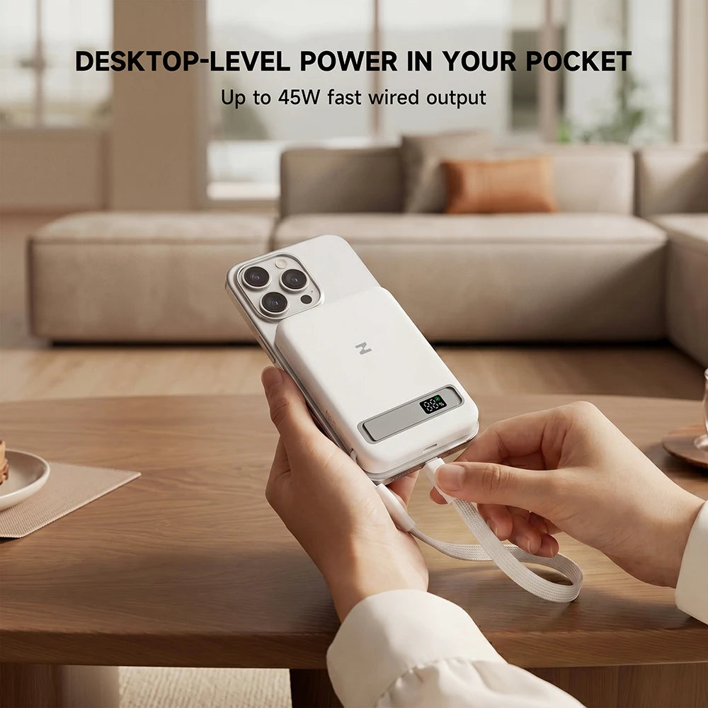 Person using a MagAir white magnetic power bank on a wooden table with a modern living room background. #color_white