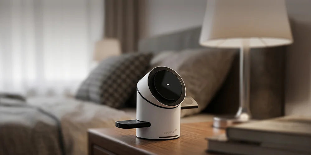 White and black ZEEHOO CylinTrick device on a nightstand with a blurred bedroom background.