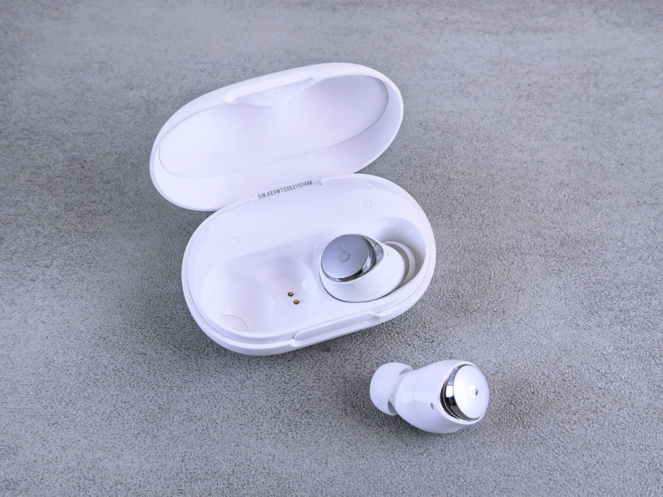 White wireless earbuds with charging case on gray background