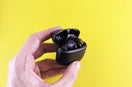Hand holding black wireless earbuds in open case.