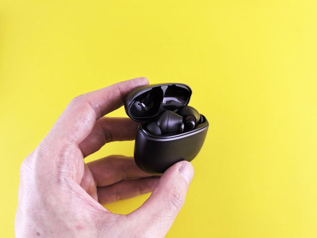 Hand holding black wireless earbuds in open case.