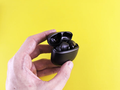 Hand holding black wireless earbuds in open case.