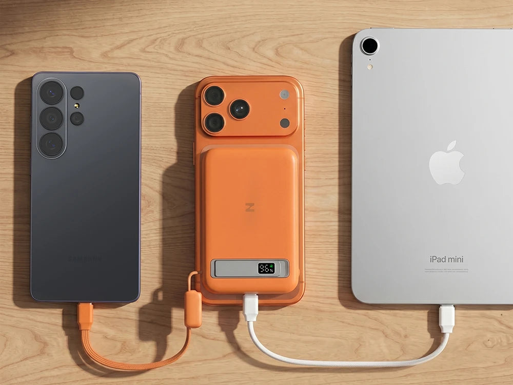 Orange power bank charging a smartphone and iPad mini on a wooden surface