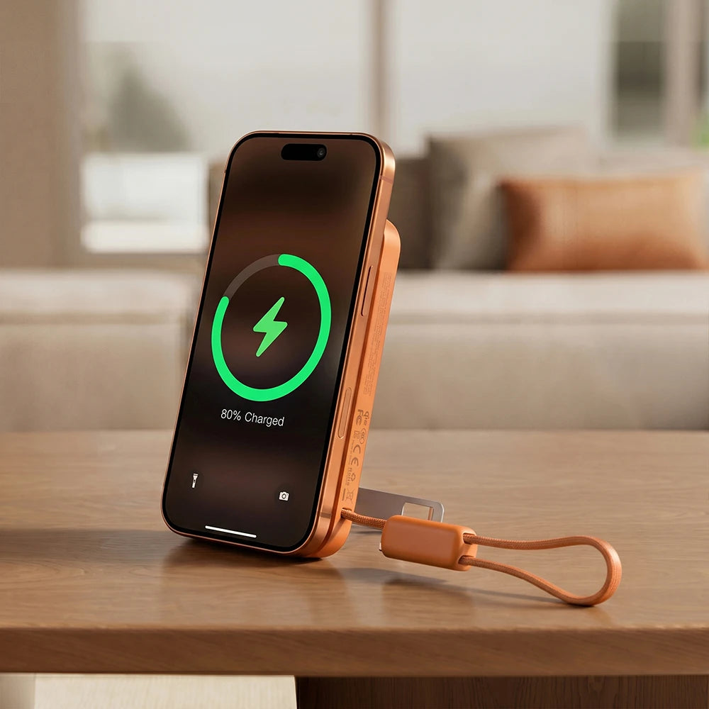 Orange smartphone with MagAir magnetic wireless power bank on a wooden table in a living room setting.