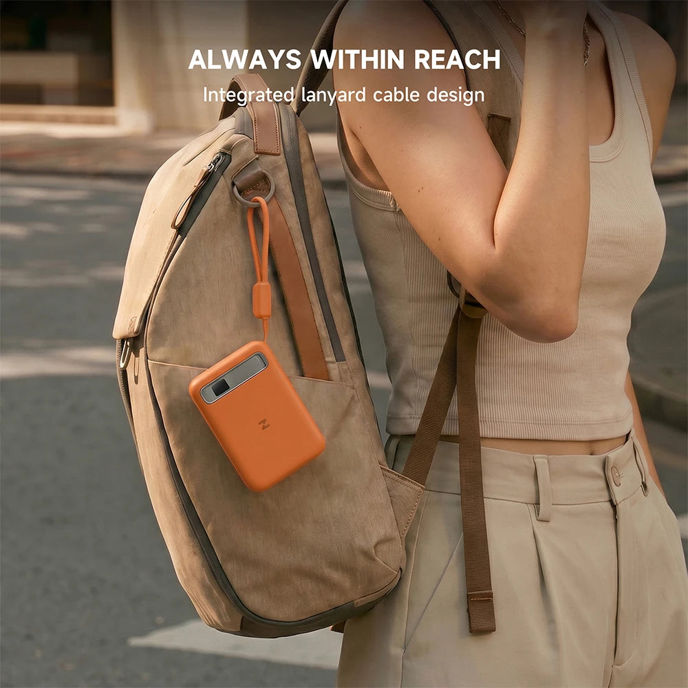Person wearing a beige backpack with an orange MagAir semi-solid-state power bank attached, on a blurred street background. #color_orange